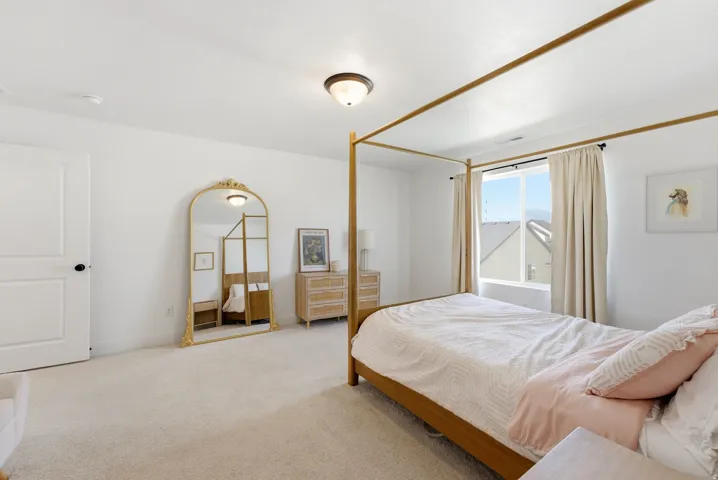 Carpeted bedroom featuring a large window with mountain scenery, white walls, a flush-mount ceiling light fixture, and a solid white door with black hardware