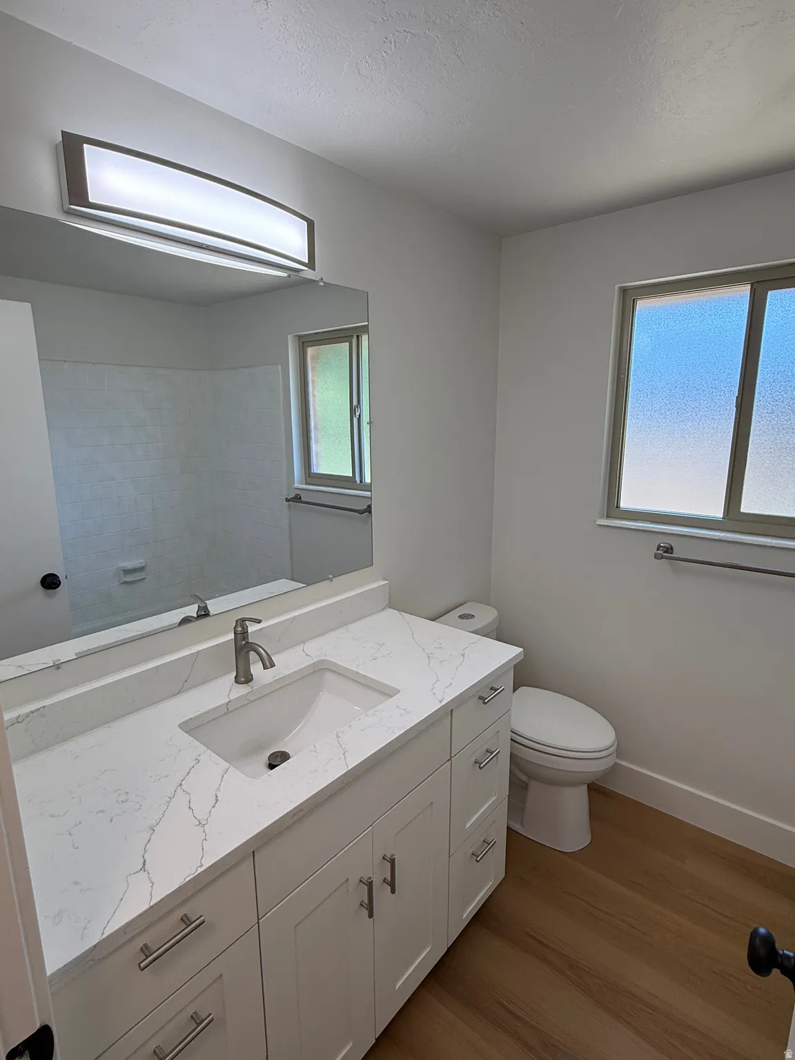 Bathroom featuring a white vanity with an undermount sink, a stone-finish countertop, and wood-finish flooring