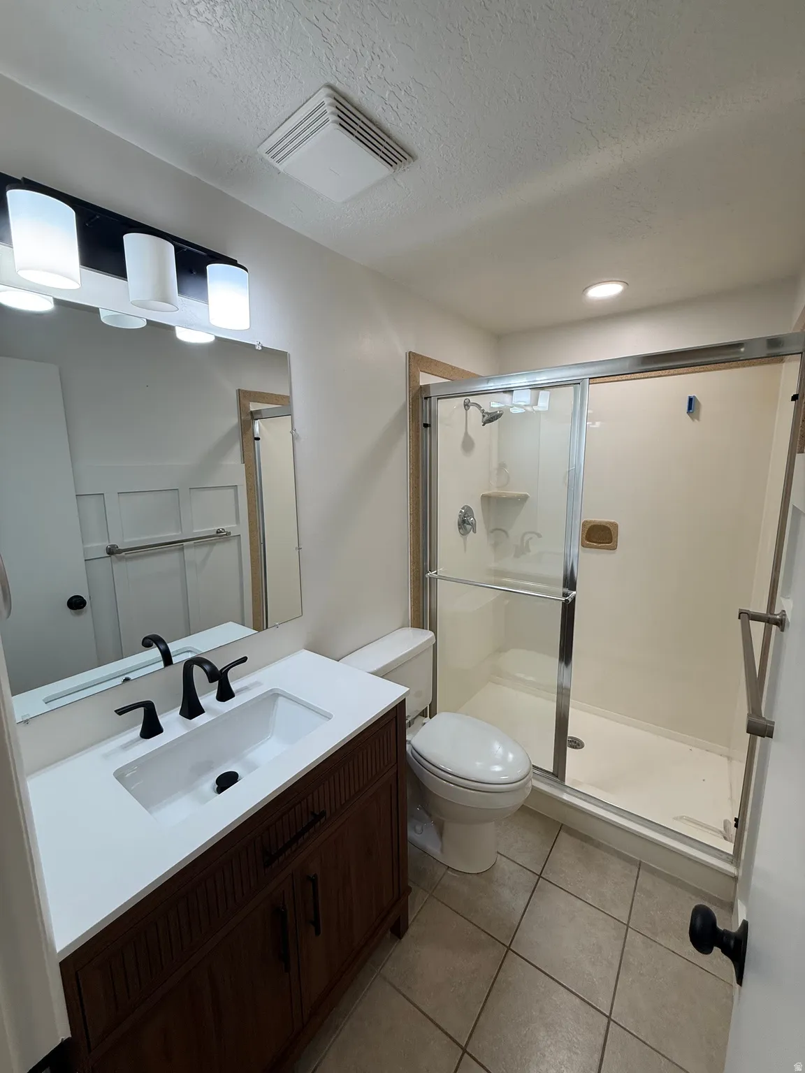 Bathroom featuring a dark wood-finish vanity with a white countertop and integrated sink, matte black faucet, and a frameless mirror