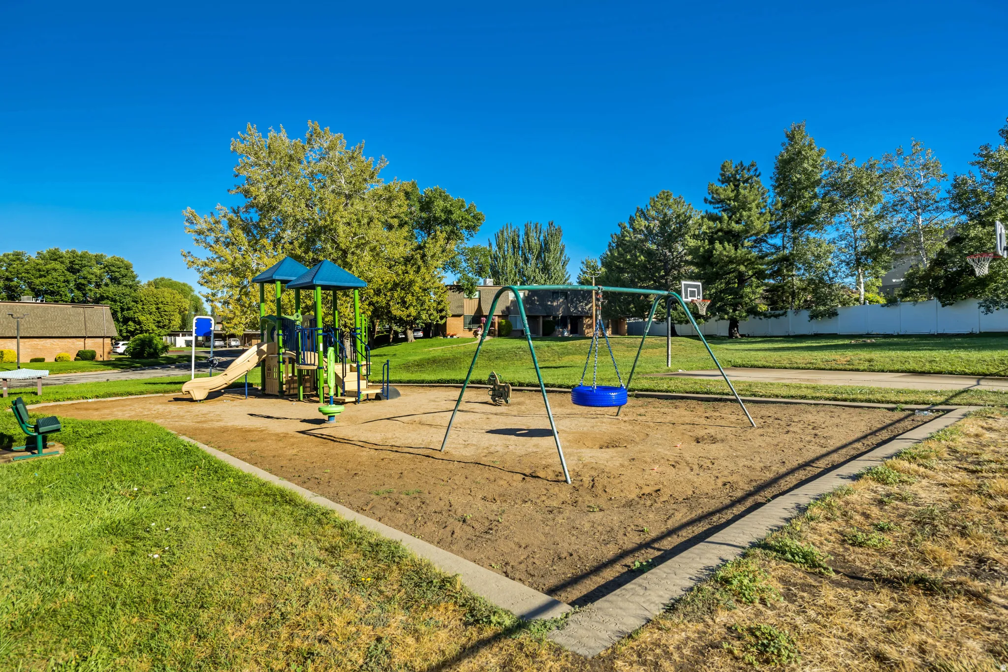 Community playground featuring a multi-level play structure with slide, a swing set, and a sand base