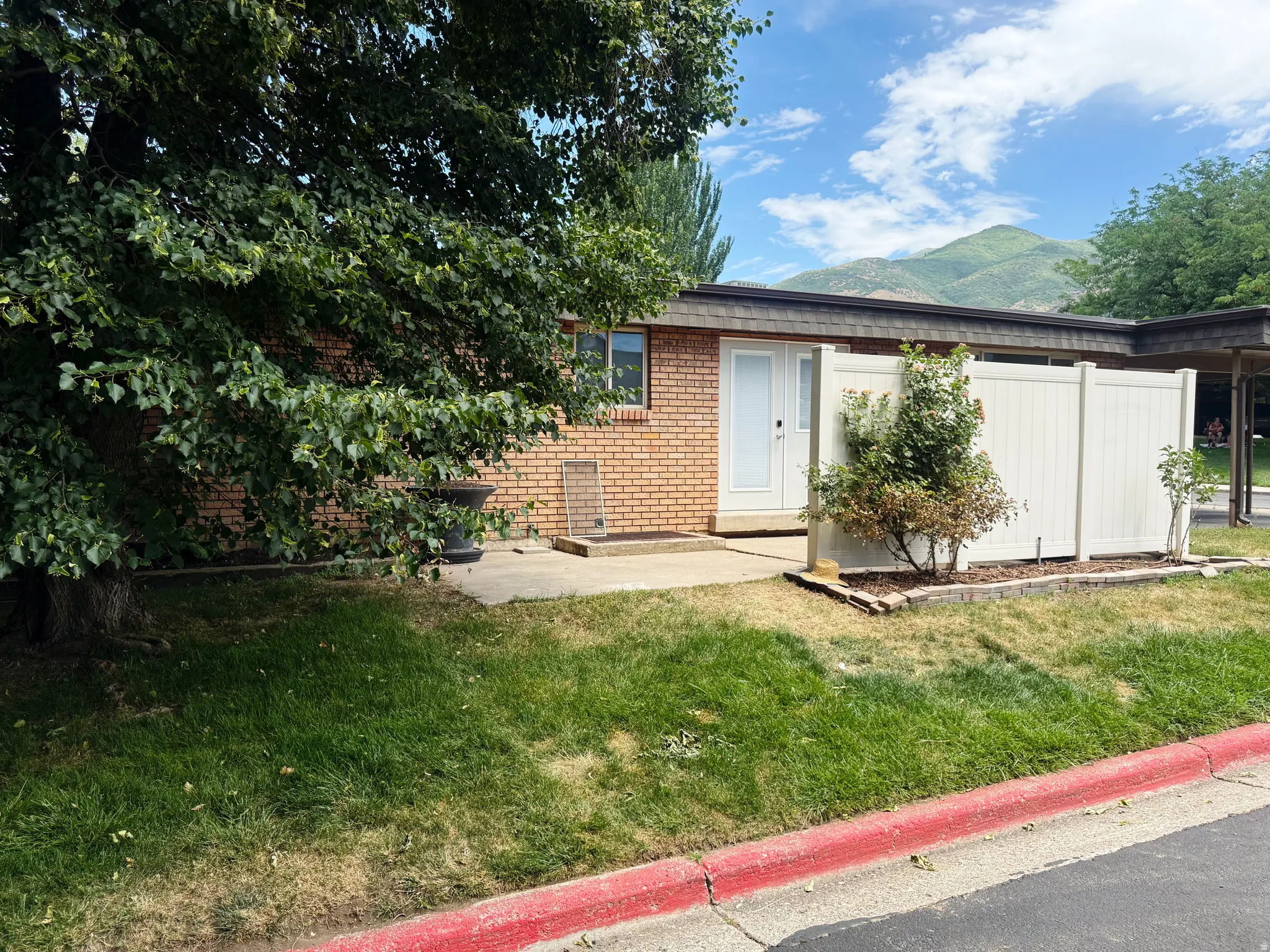 Brick facade property with a white entry door, framed by a mature shade tree and a white privacy fence