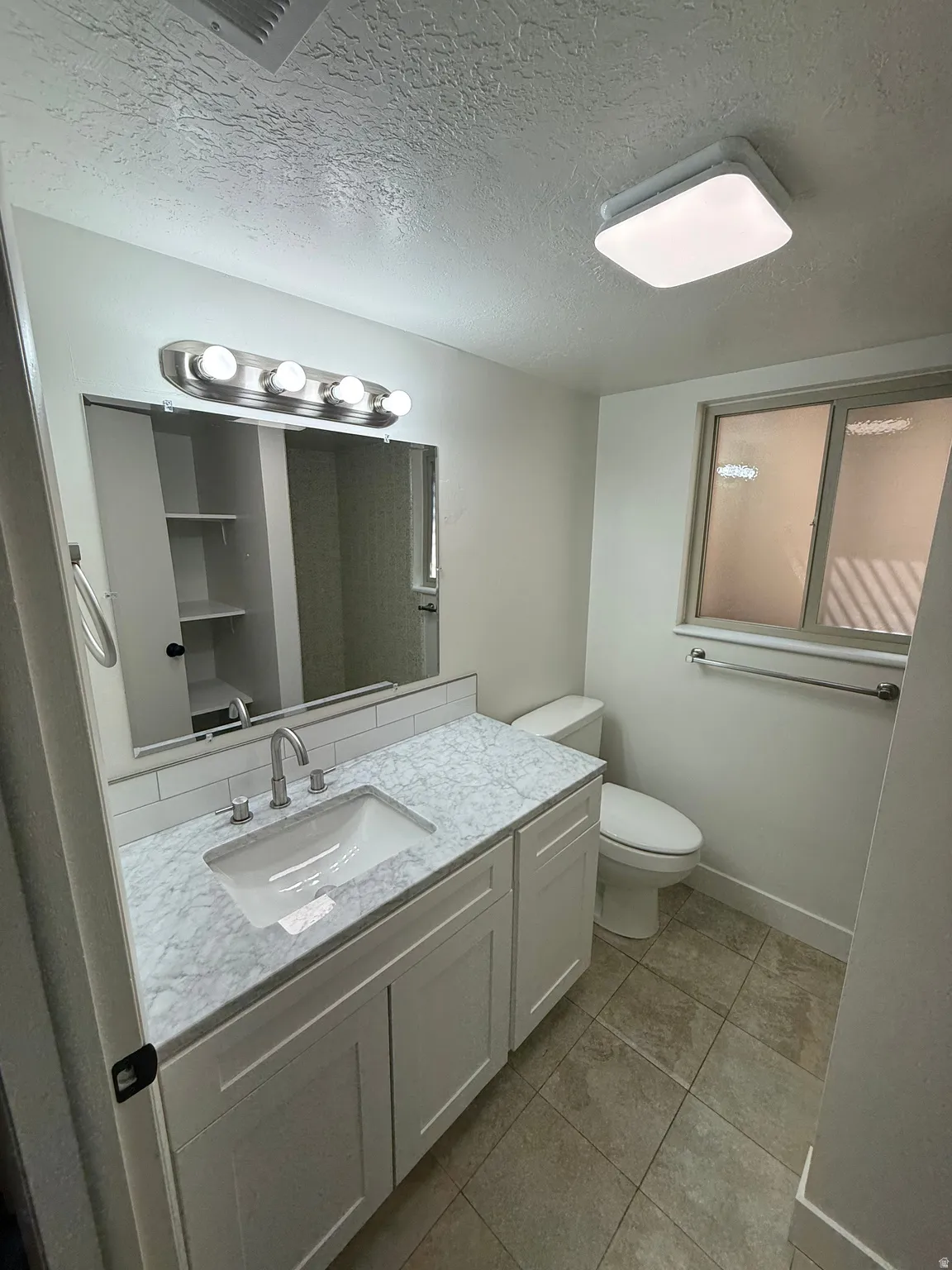Bathroom featuring a single vanity with stone-finish countertop, undermount sink, and white shaker-style cabinetry