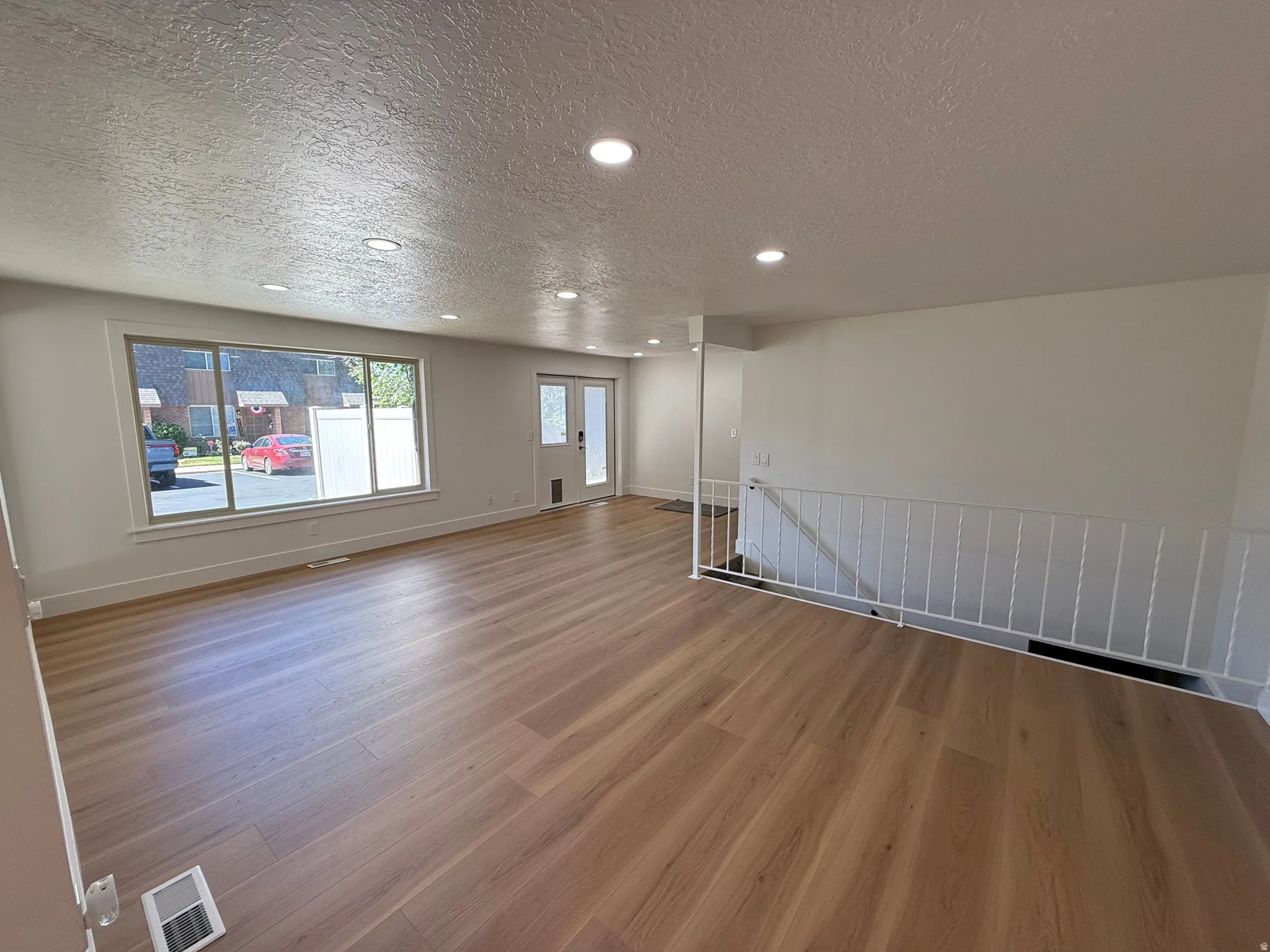 Expansive main living area featuring wood-finish flooring, a large picture window, recessed lighting, and a white staircase railing