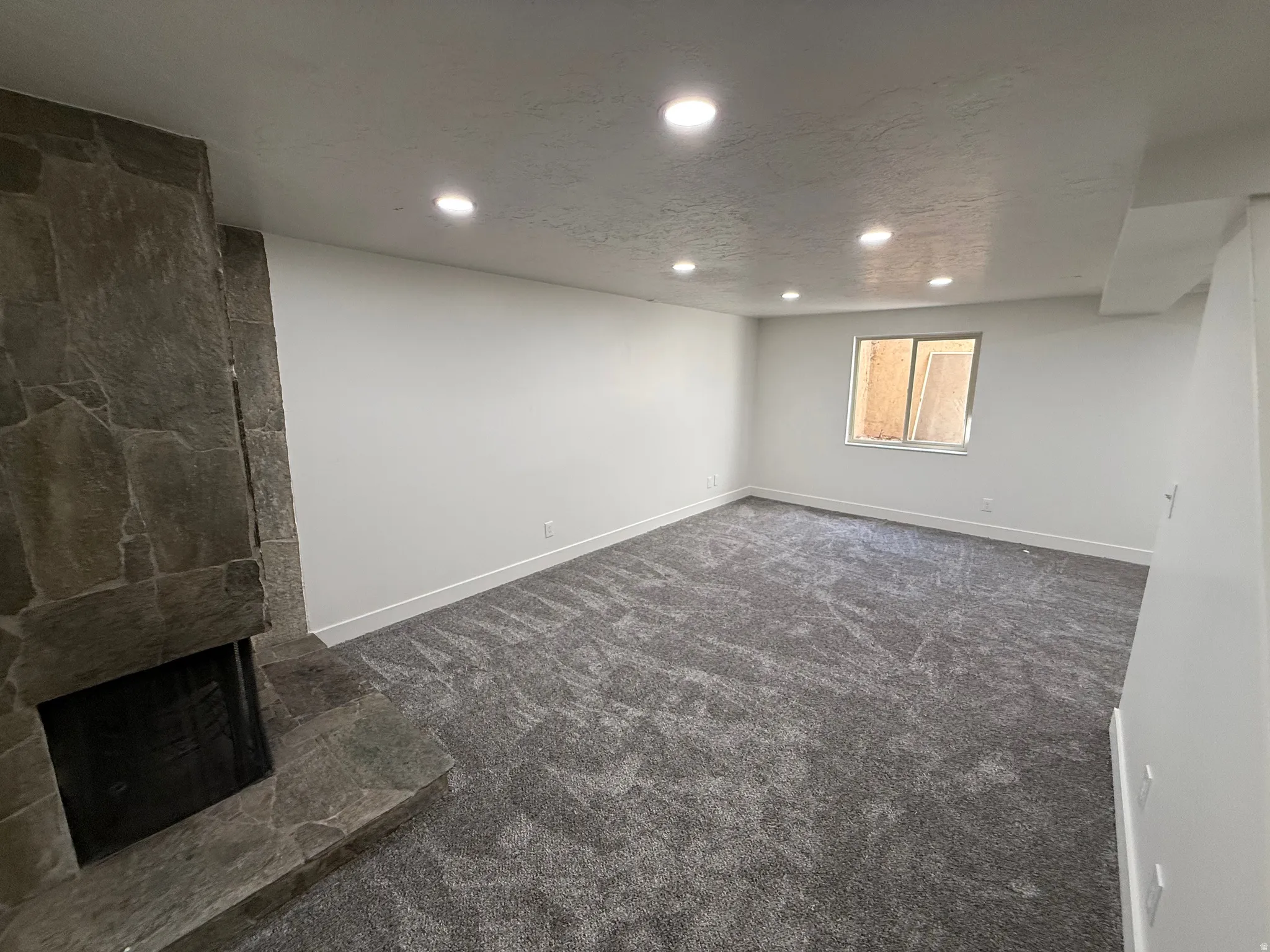 Spacious room featuring a stone-clad fireplace with a hearth, recessed lighting, neutral wall tones, and plush patterned carpeting