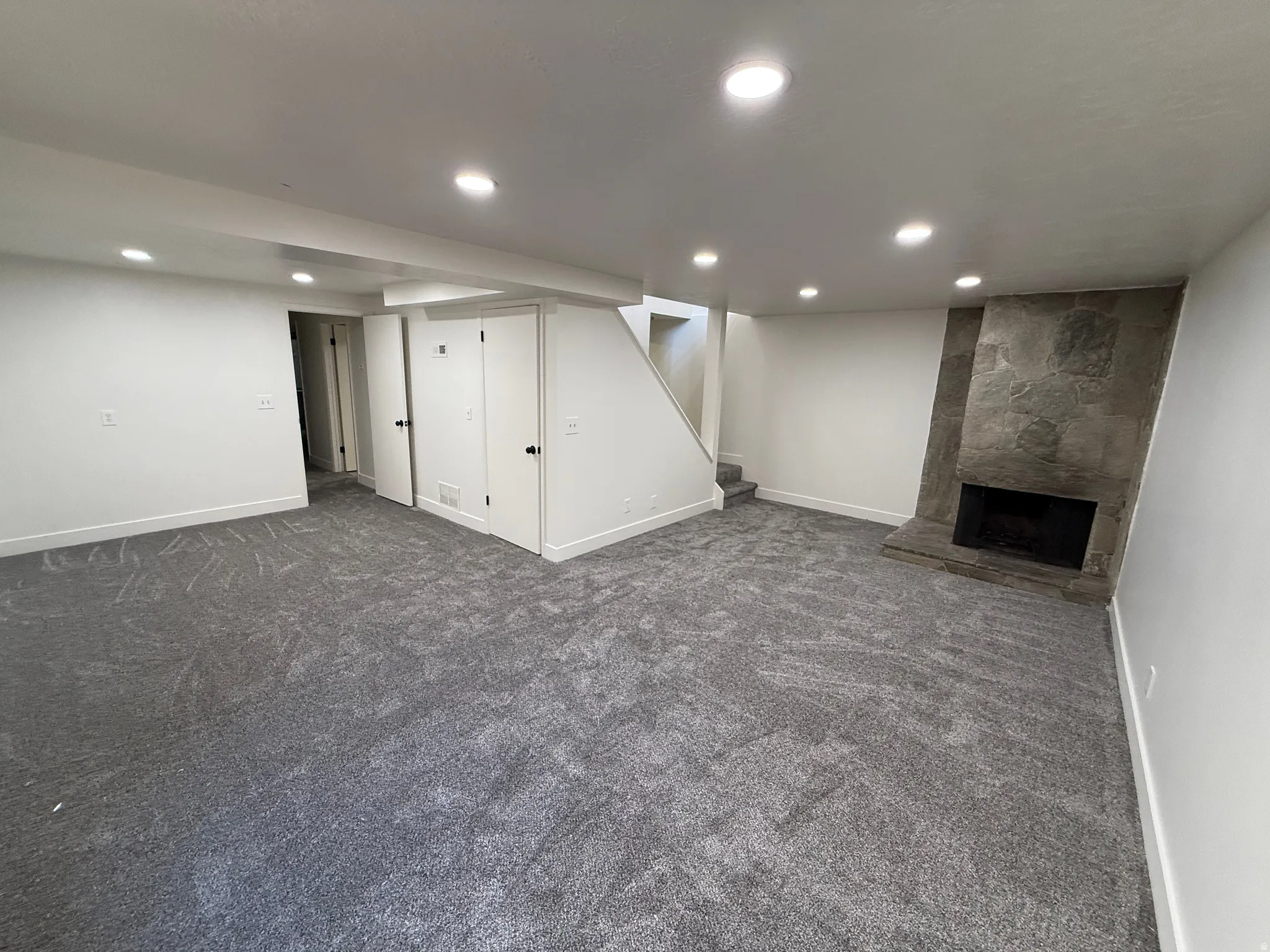 Spacious room featuring gray patterned carpet, recessed lighting, white walls, and a stone-clad fireplace