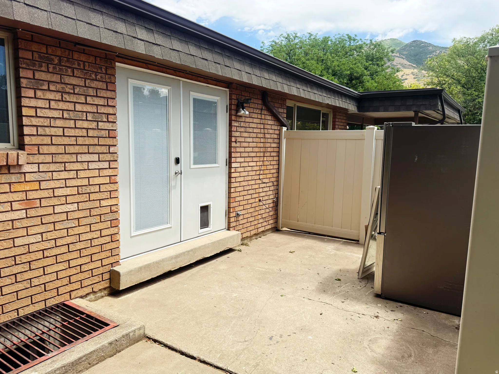 Brick exterior with twin light-paneled doors, concrete patio, and a privacy fence