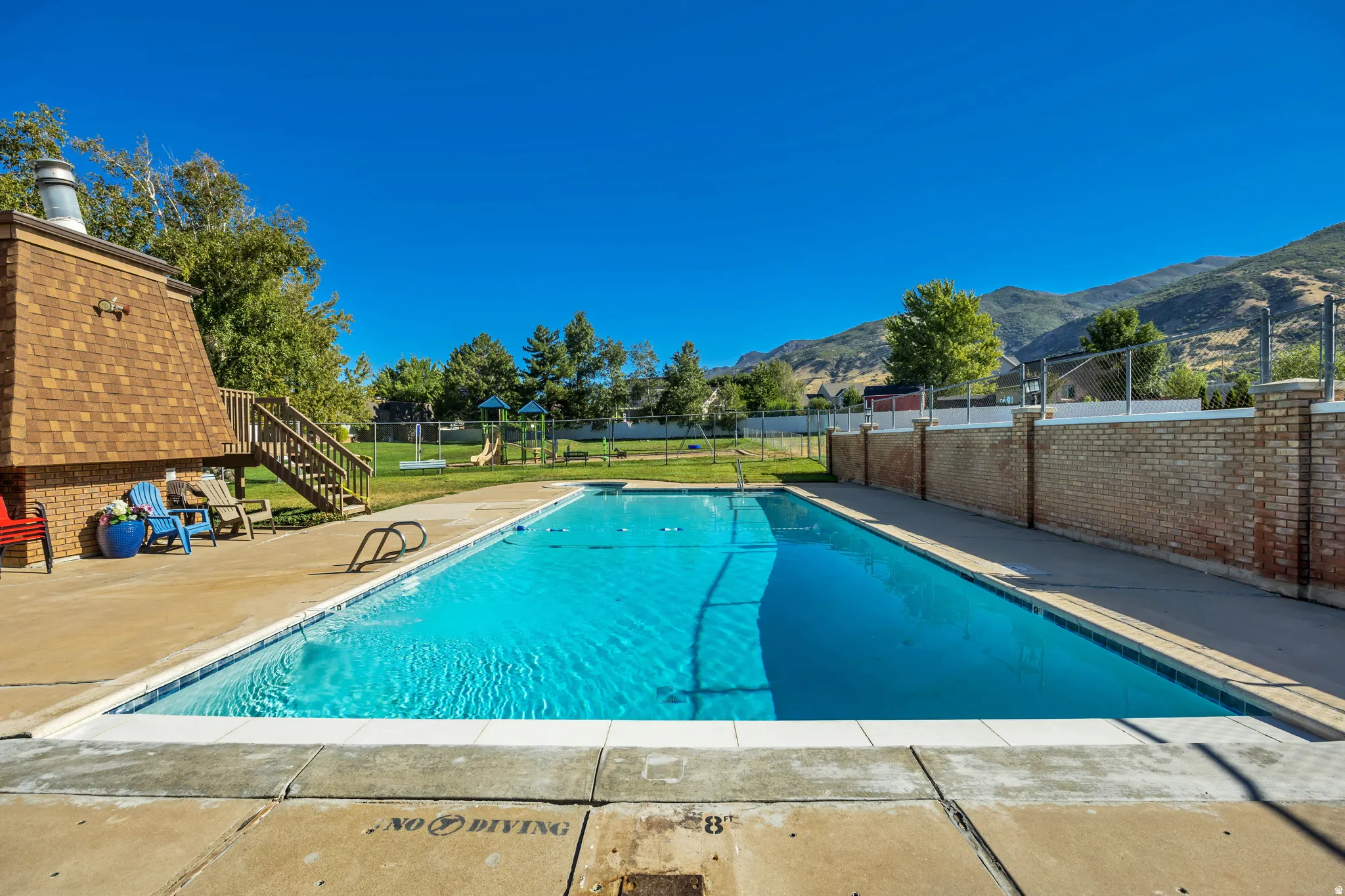 Outdoor swimming pool with concrete decking, a brick privacy wall, and mountain scenery