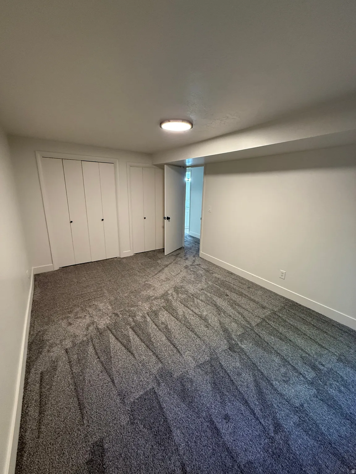 Spacious room featuring new gray patterned carpet, white walls, two bi-fold closet doors, and a ceiling-mounted light fixture