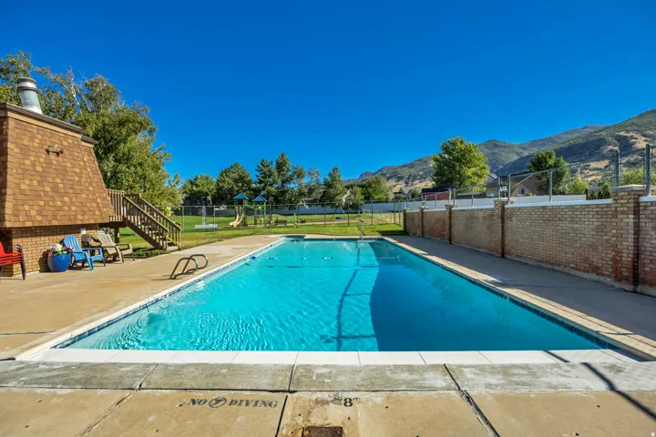Outdoor swimming pool with concrete decking, a brick privacy wall, and mountain scenery