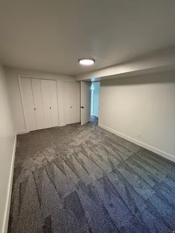 Spacious room featuring new gray patterned carpet, white walls, two bi-fold closet doors, and a ceiling-mounted light fixture