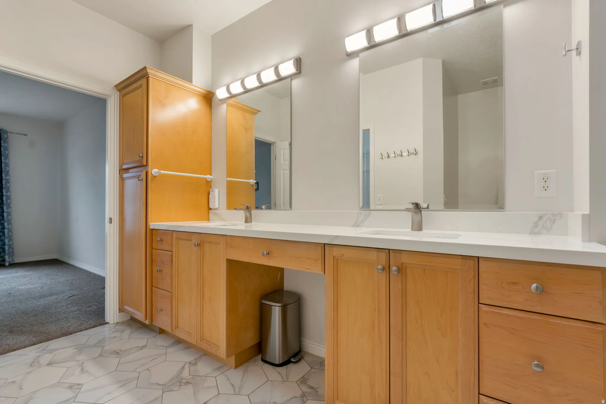 Bathroom featuring a dual vanity with light wood cabinetry, white stone countertops, and integrated sinks