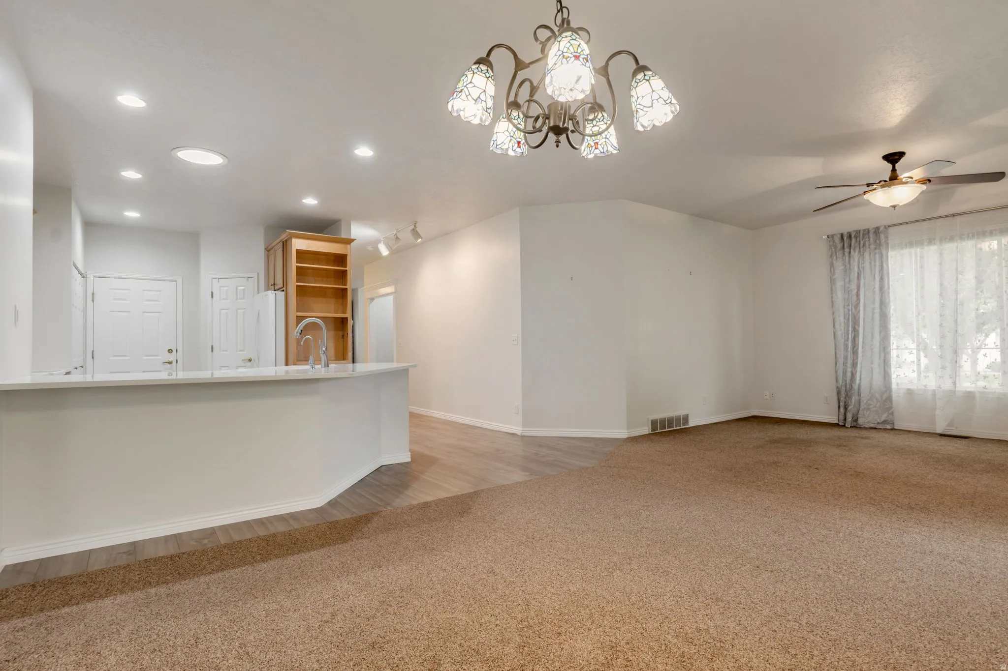Open living area featuring recessed lighting, a decorative chandelier, a ceiling fan, and mixed flooring with wood-finish planks and carpet. ROOM for barstools