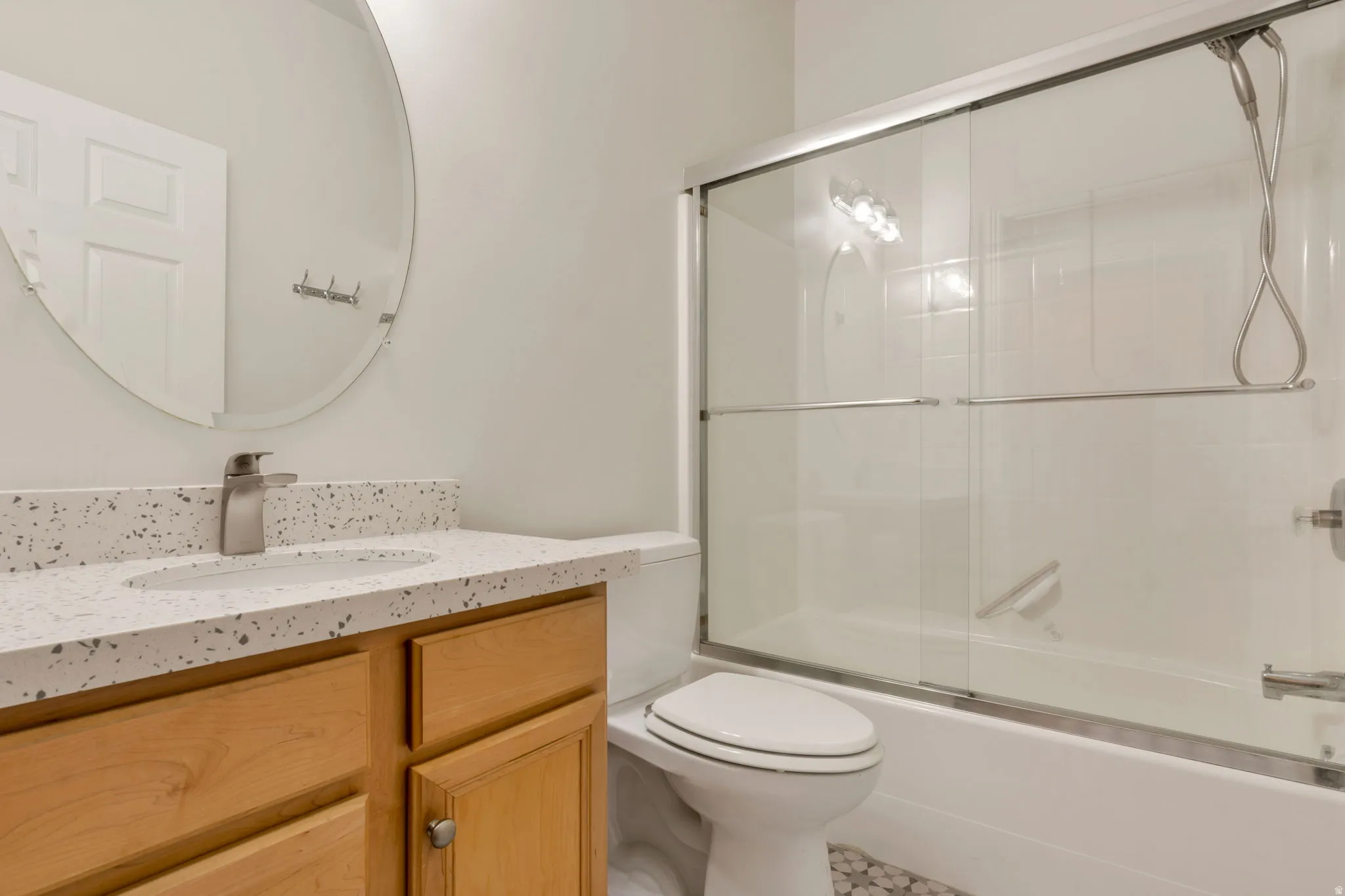 Guest Bathroom featuring a light wood vanity, speckled white countertop with integrated sink, and a brushed nickel faucet