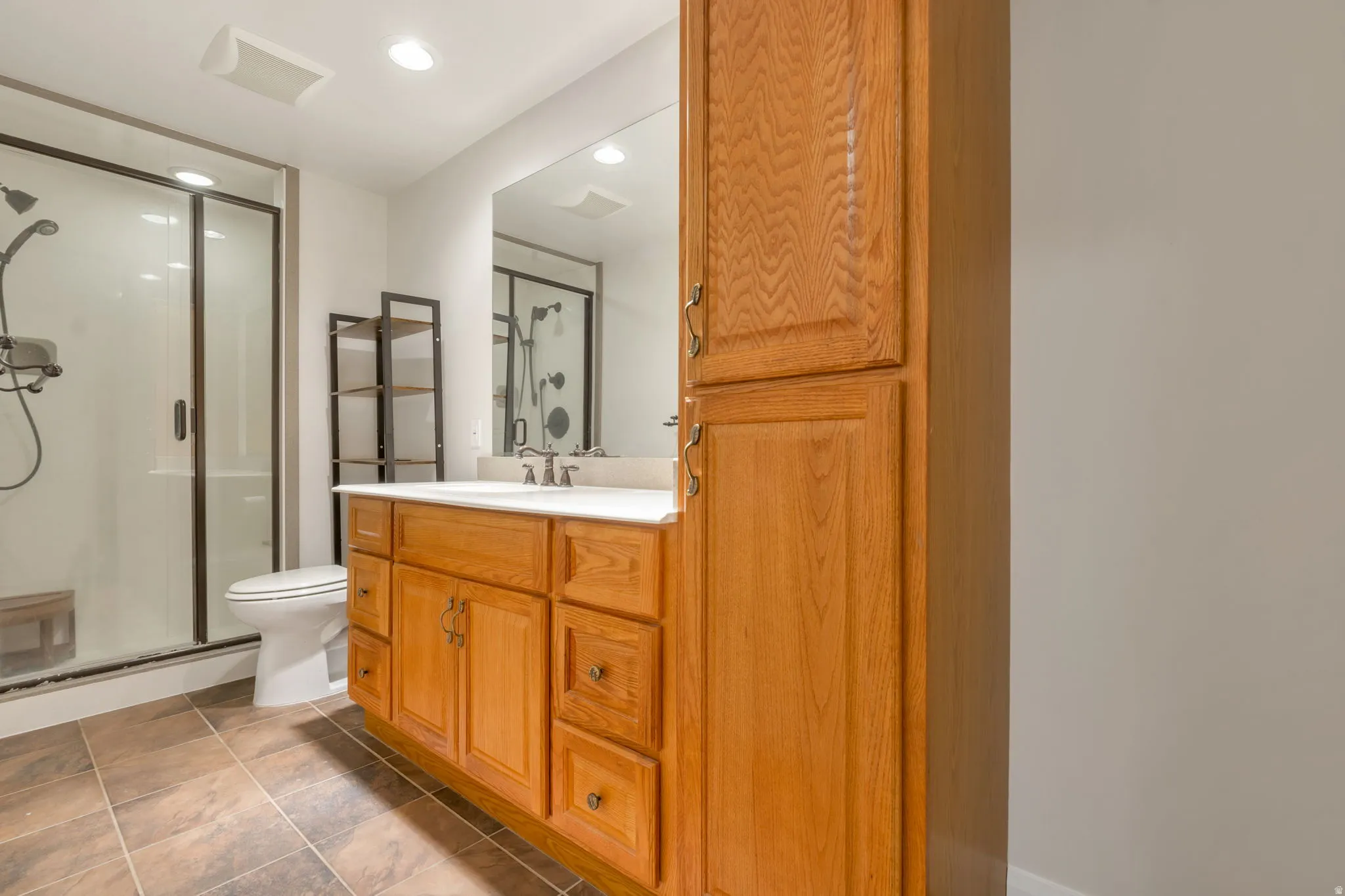Bathroom featuring a wood vanity with a white countertop, large mirror, tile flooring, and a glass-enclosed shower