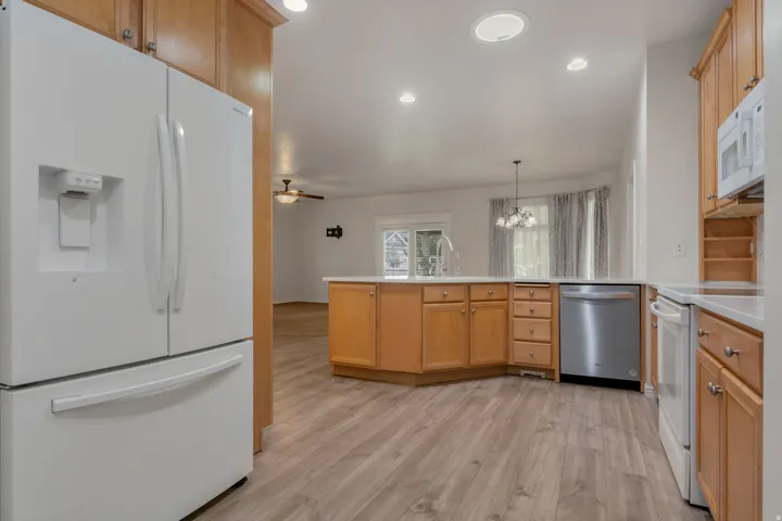 Kitchen entry from garage,  featuring wood-finish flooring, recessed lighting, and a center island with sink and integrated dishwasher