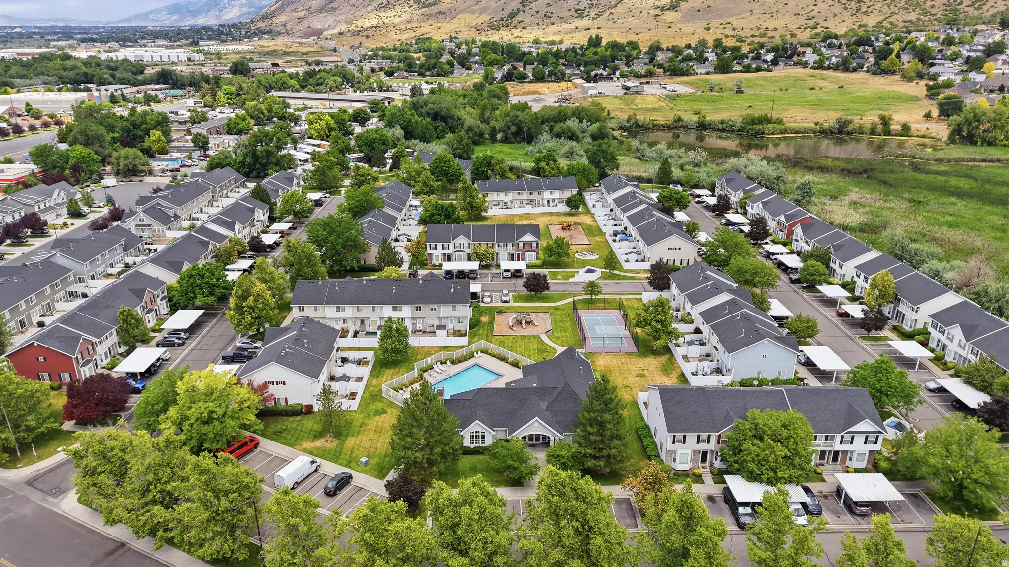 Aerial overview of a multi-unit residential community featuring a central swimming pool, tennis court, and playground