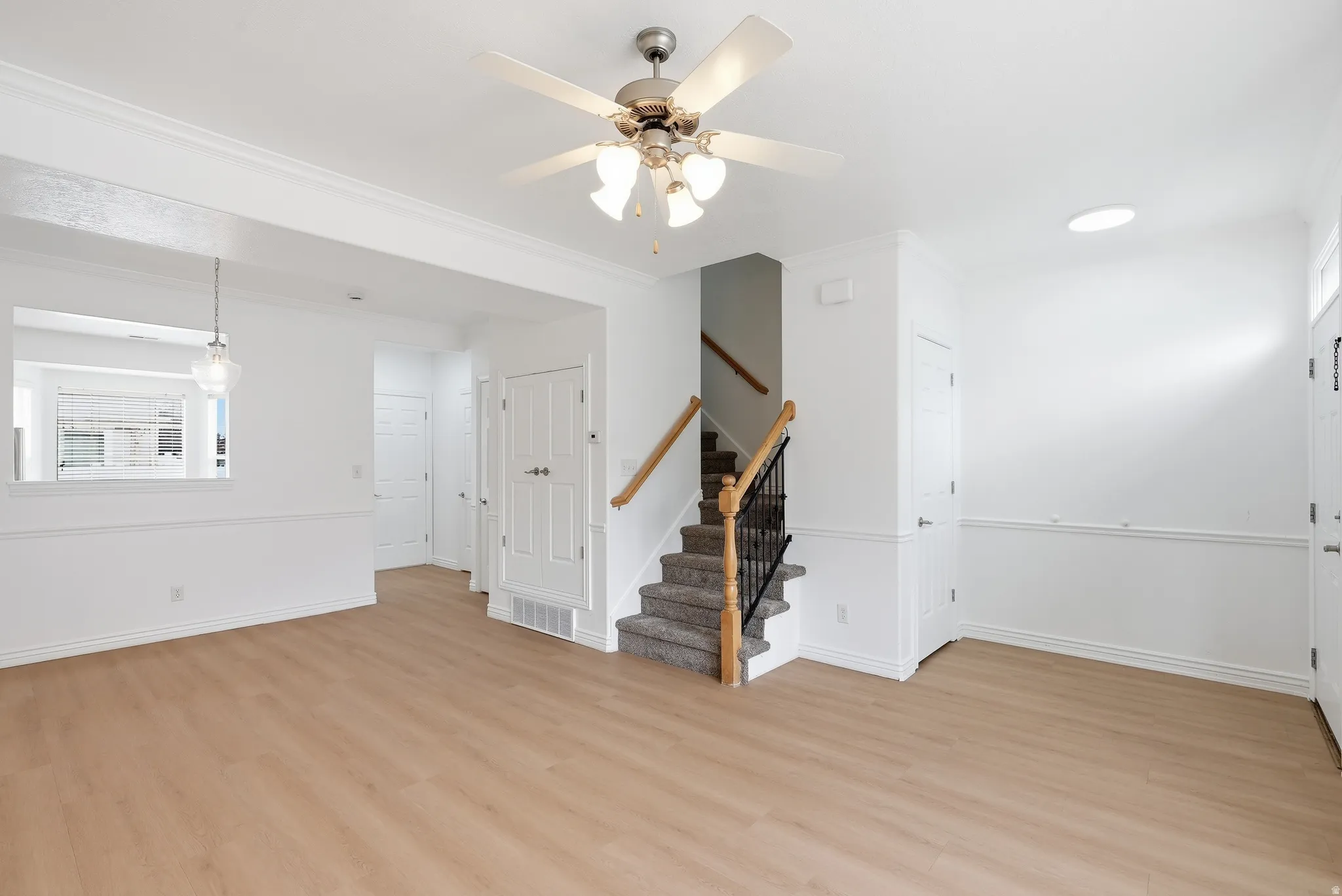 Open-concept living space with light wood-finish flooring, white walls, and crown molding