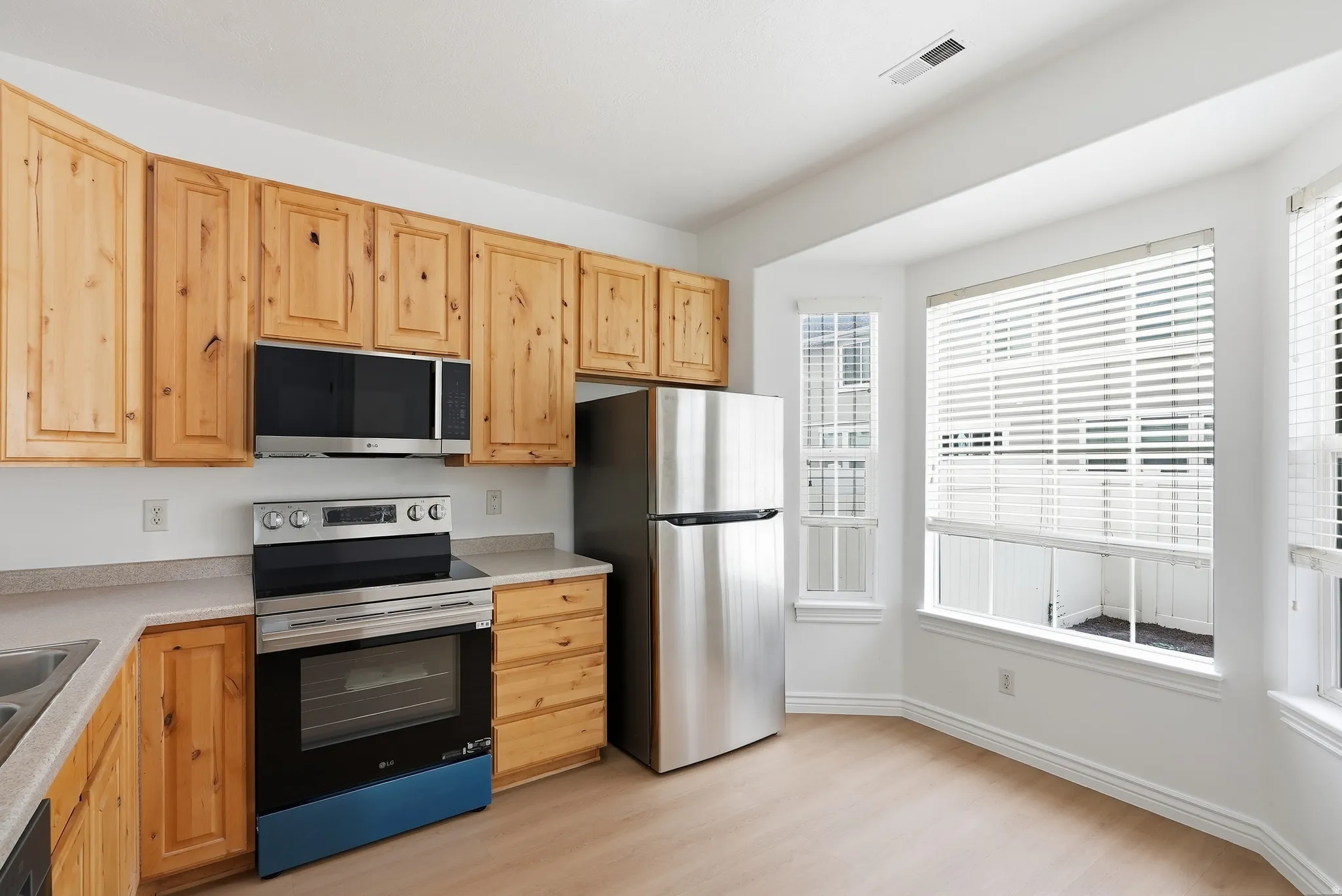 Kitchen featuring natural wood cabinetry, light-toned countertops, and stainless steel appliances including a refrigerator, range, and microwave