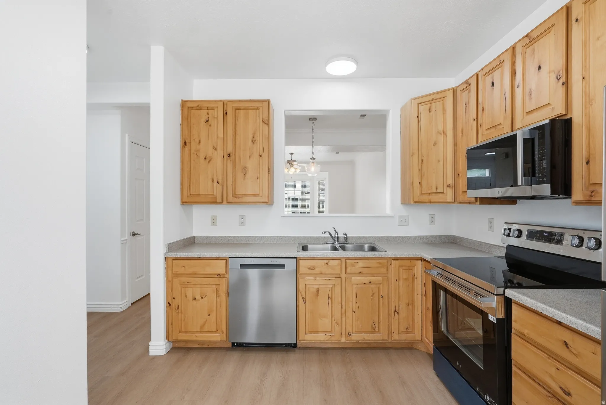 Kitchen featuring natural wood cabinetry, light grey countertops, stainless steel appliances, and a wood-finish floor