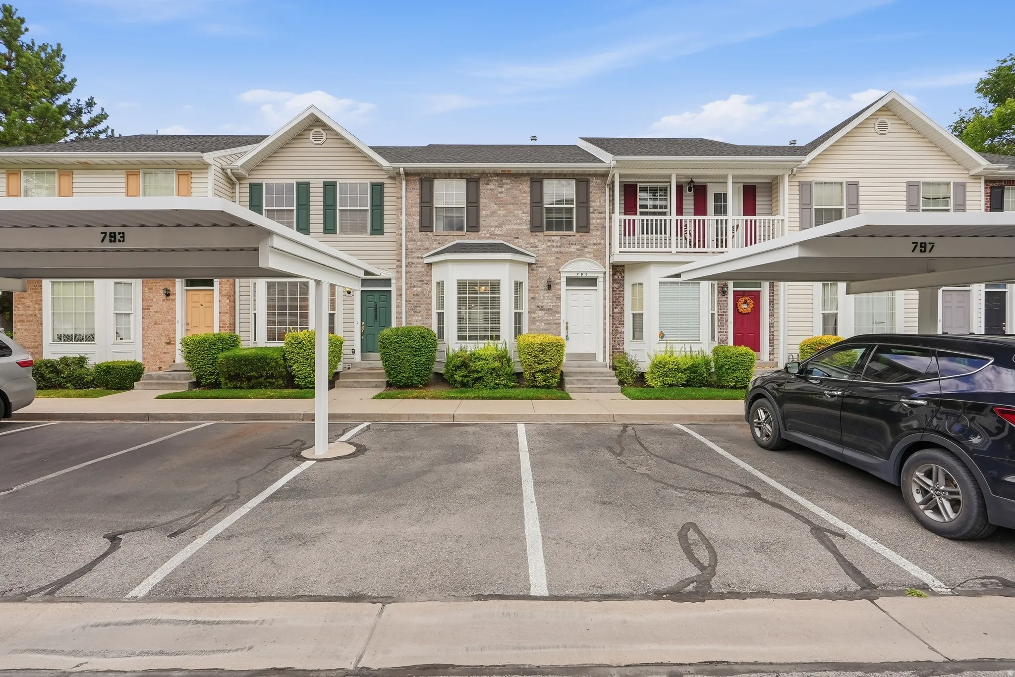 Townhome exterior featuring a combination of brick and siding, multiple windows with shutters, and mature landscaping