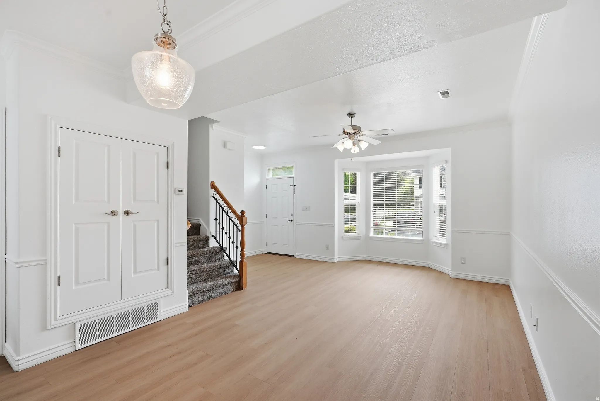 Expansive living area with light wood-finish flooring, a bay window, and a ceiling fan