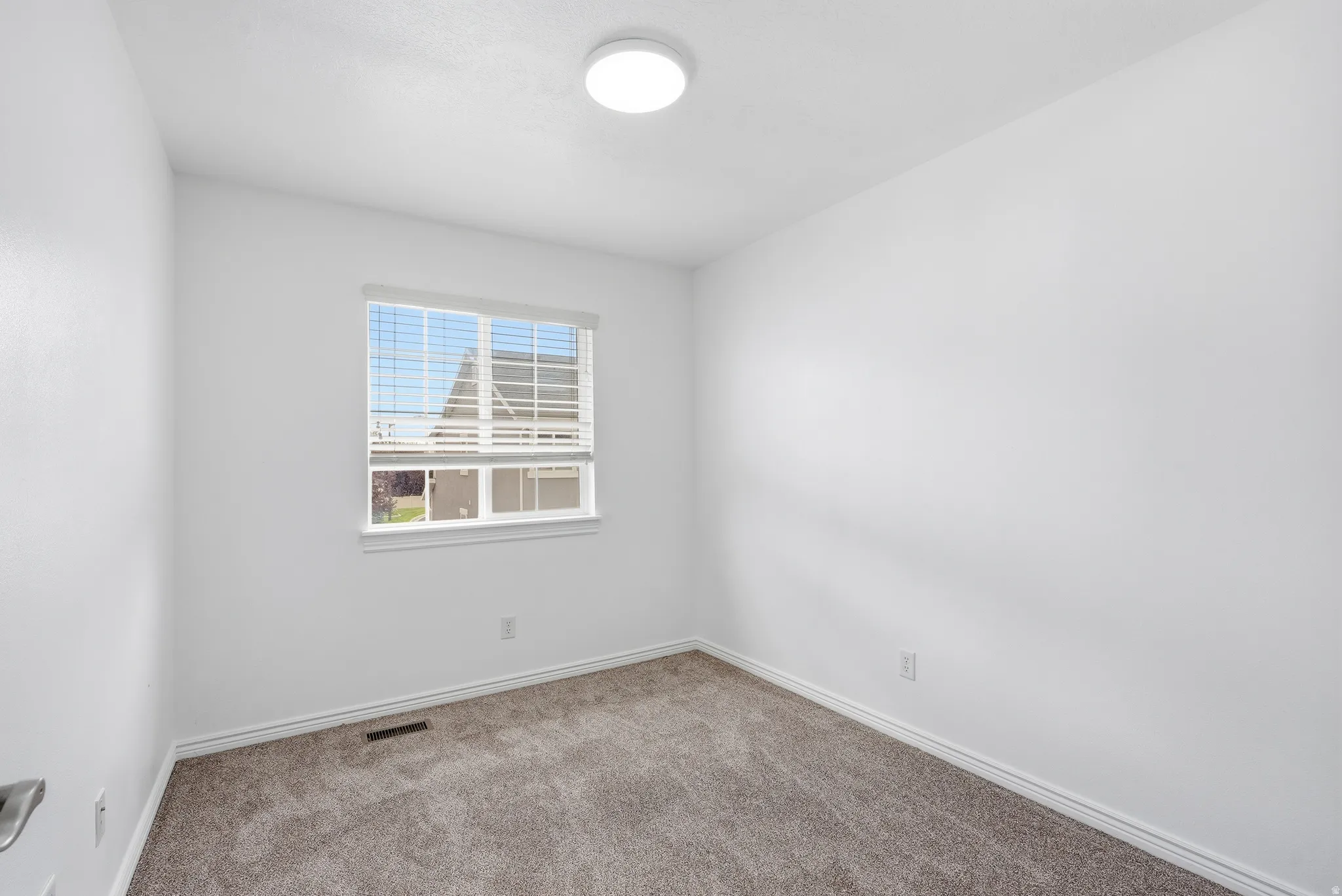 Neutral white walls with a single window featuring horizontal blinds