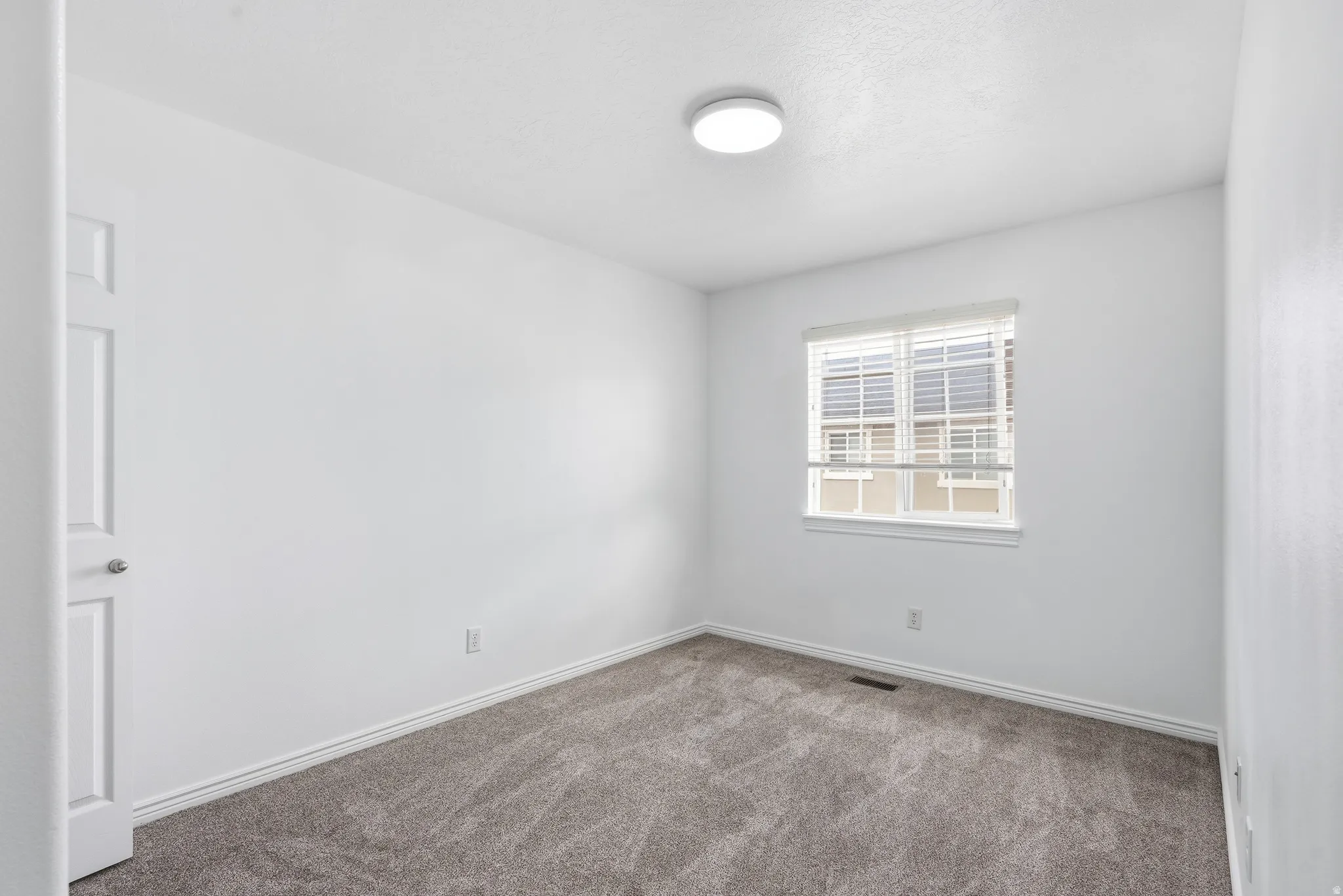 Room featuring a window with blinds, a flush mount ceiling light fixture, neutral gray carpet, and white trim