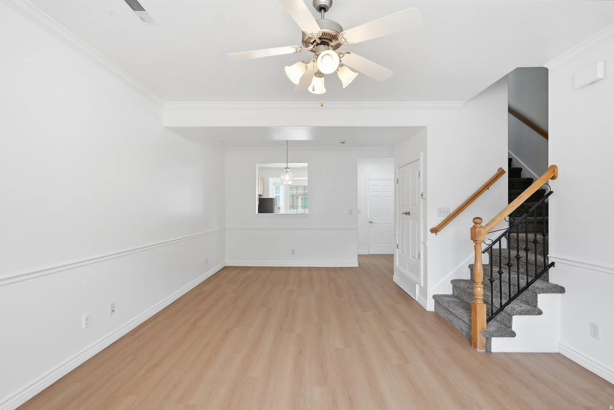 Spacious room featuring light wood-finish flooring, white crown molding, and a ceiling fan with integrated lighting