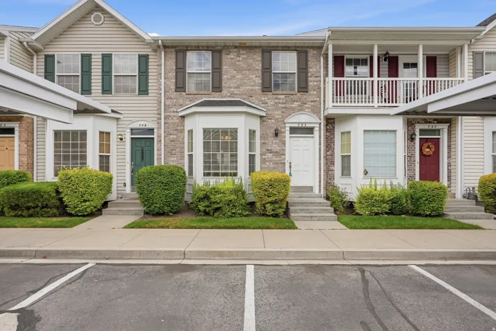 Townhome exterior featuring a mix of brick and siding, bay windows, a covered balcony with white railings, and manicured shrubbery