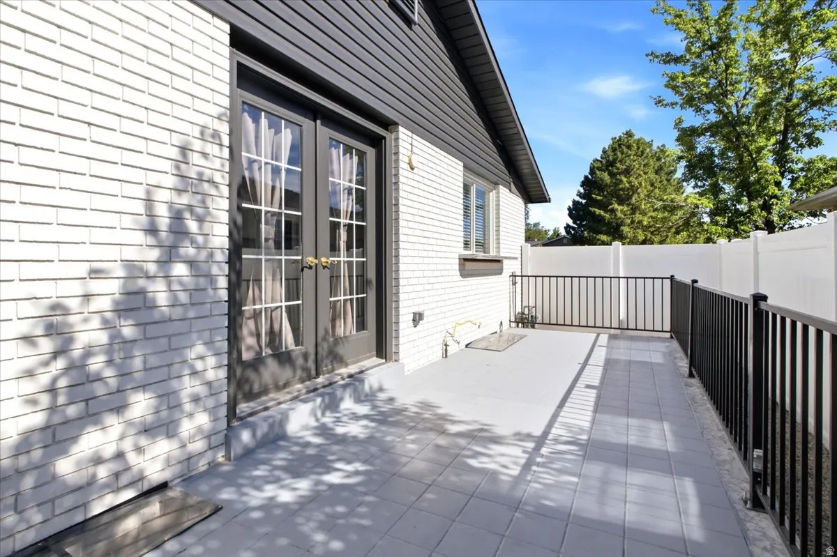 Patio featuring a durable tiled surface, black metal railing, white brick exterior, and French doors
