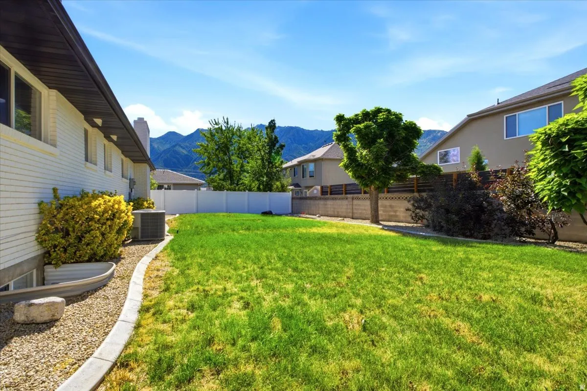 Expansive backyard featuring a lush lawn, a white privacy fence, and mature trees with great mountain views.