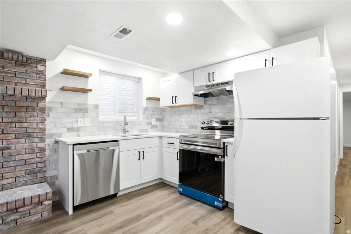 Bright  basement kitchen featuring white cabinetry, a white countertop, a tile backsplash, and stainless steel appliances