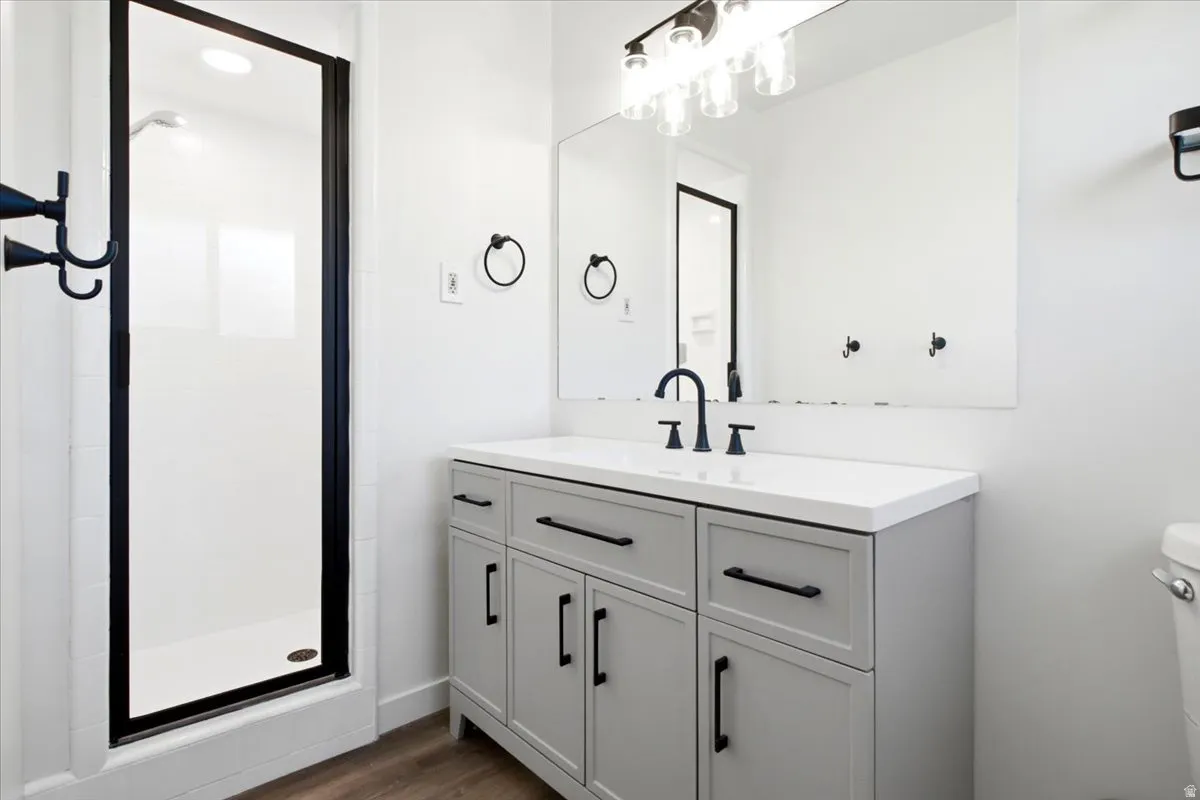Master Bathroom featuring a gray vanity with a white countertop, matte black fixtures, a shower with a black-framed glass enclosure, and wood-finish flooring