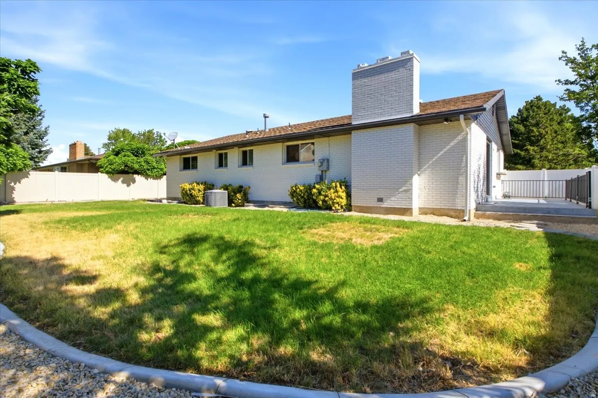 Expansive backyard featuring a manicured lawn, white brick exterior, a substantial white brick chimney, a privacy fence, and a concrete patio with a modern railing system