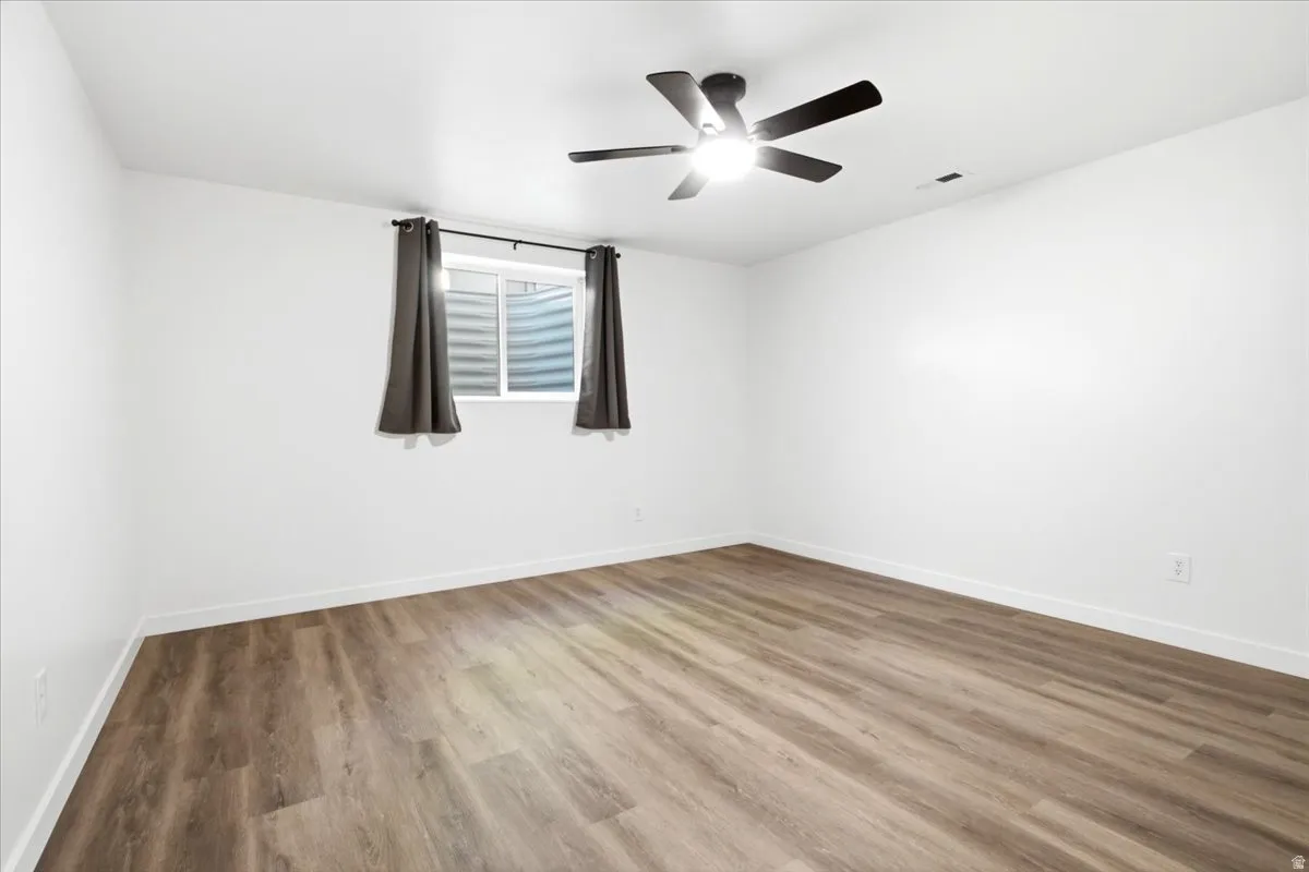 Spacious room featuring wood-finish flooring, white baseboards, and a modern ceiling fan with integrated lighting