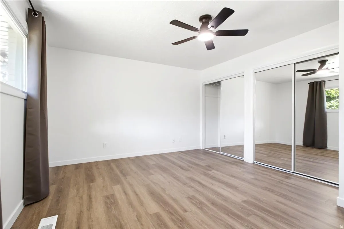Master bedroom featuring wood-finish flooring, a contemporary ceiling fan, and large mirrored closet doors