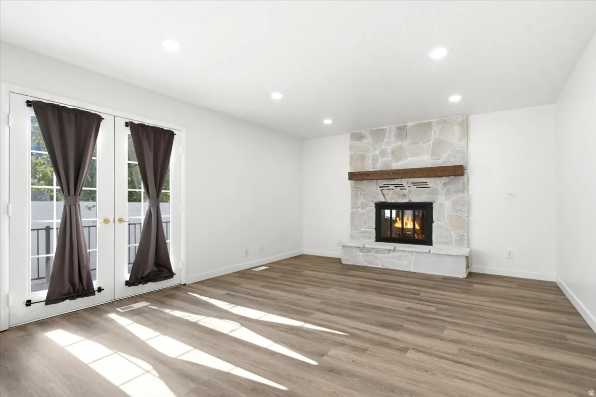 Living area featuring a stone-clad fireplace with a wood mantel, dual French doors with clear glass panes, light wood-finish flooring, recessed lighting, and white walls