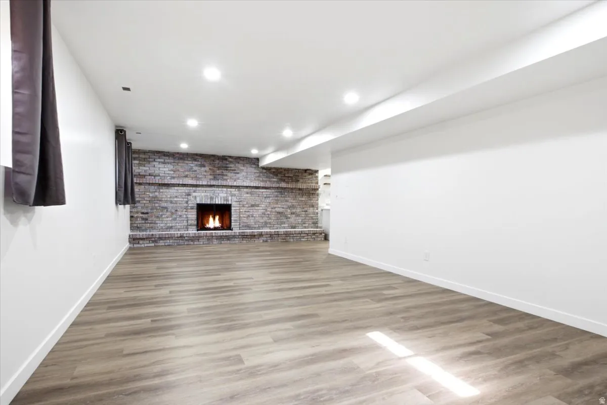 Spacious room featuring wood-finish flooring, recessed lighting, and a prominent brick fireplace