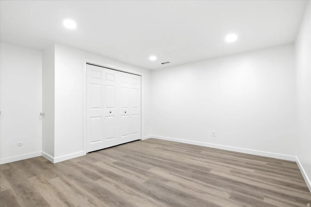 Spacious room featuring wood-finish flooring, recessed lighting, white walls, white baseboards, and bi-fold closet doors