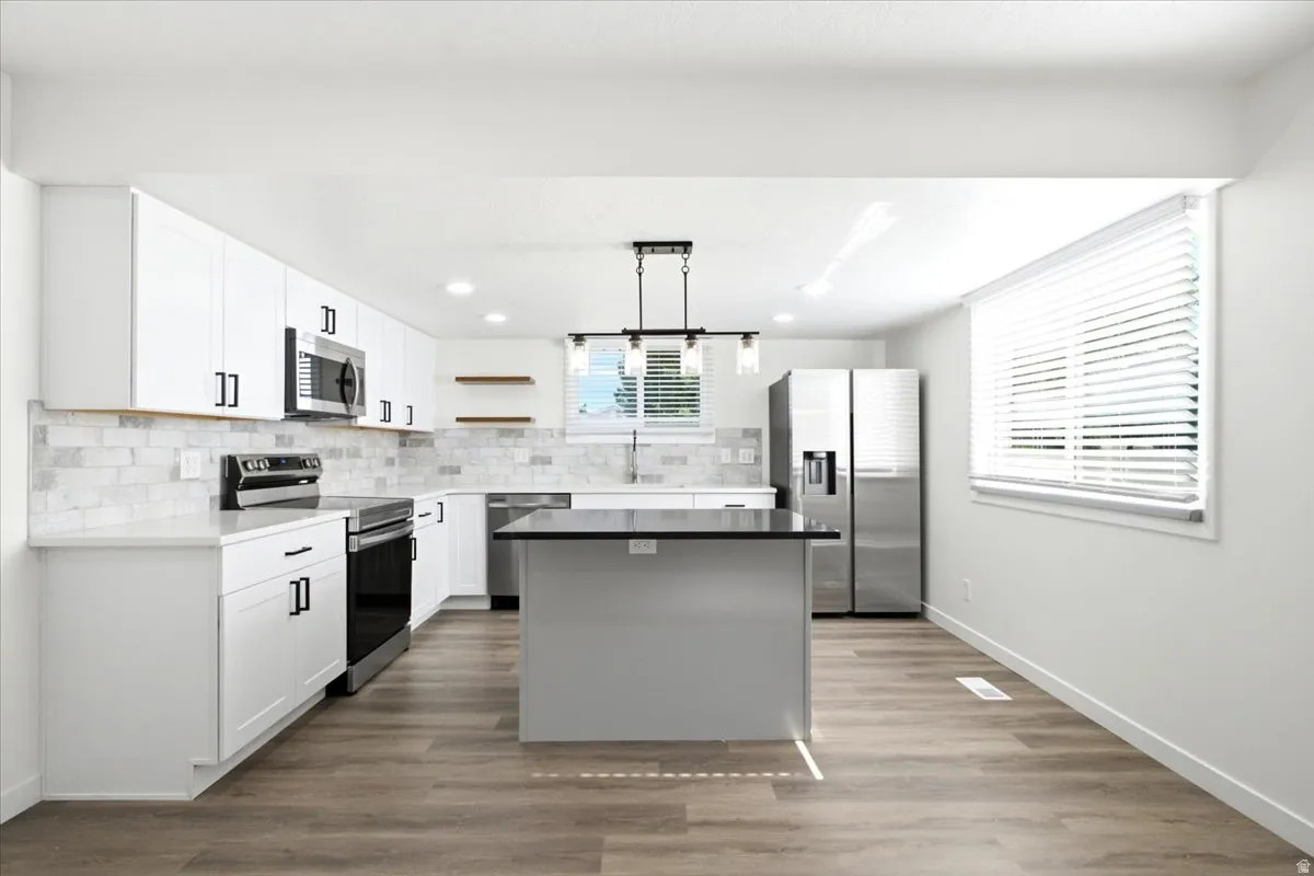 Modern kitchen featuring white cabinetry, a dark island with a contrasting countertop, stainless steel appliances, wood-finish flooring, and a subway tile backsplash