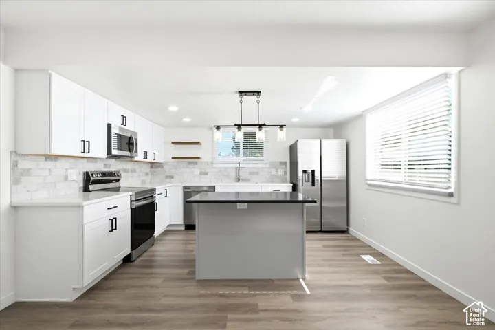 Modern kitchen featuring white cabinetry, a dark island with a contrasting countertop, stainless steel appliances, wood-finish flooring, and a subway tile backsplash