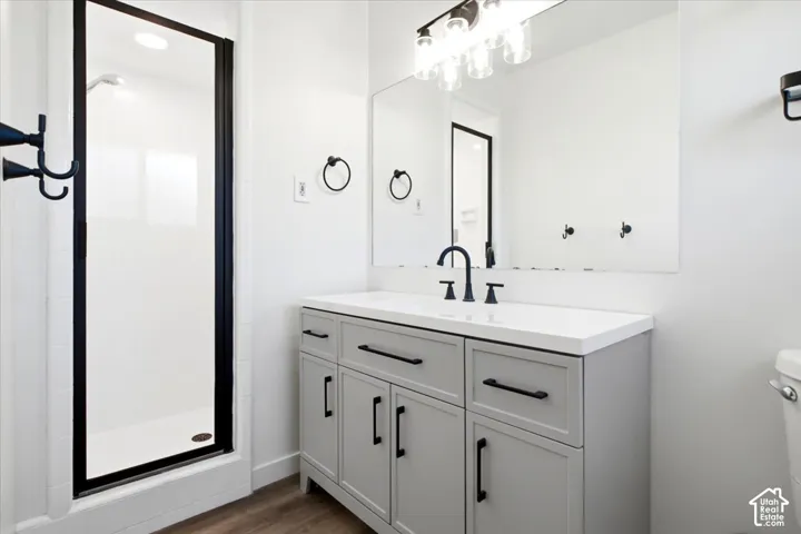 Master Bathroom featuring a gray vanity with a white countertop, matte black fixtures, a shower with a black-framed glass enclosure, and wood-finish flooring