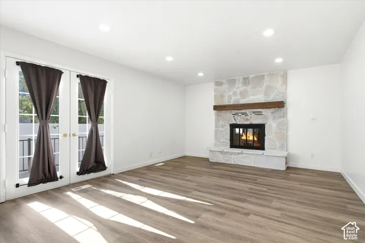 Living area featuring a stone-clad fireplace with a wood mantel, dual French doors with clear glass panes, light wood-finish flooring, recessed lighting, and white walls