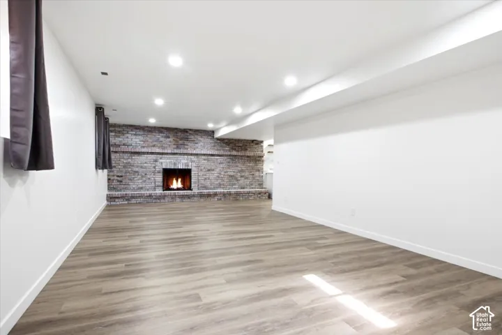 Spacious room featuring wood-finish flooring, recessed lighting, and a prominent brick fireplace