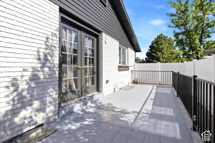 Patio featuring a durable tiled surface, black metal railing, white brick exterior, and French doors