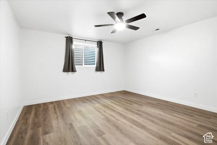 Spacious room featuring wood-finish flooring, white baseboards, and a modern ceiling fan with integrated lighting