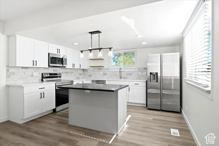 Kitchen featuring white shaker cabinetry, stainless steel appliances, a center island with a dark countertop, wood-finish flooring, and a subway tile backsplash
