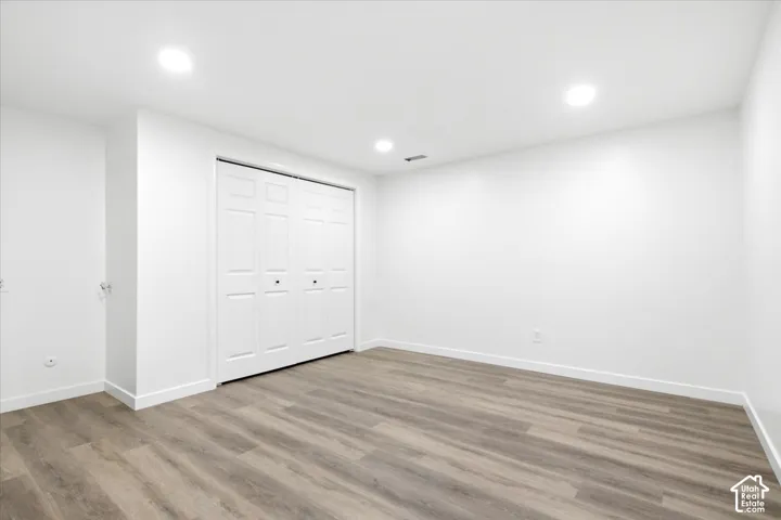 Spacious room featuring wood-finish flooring, recessed lighting, white walls, white baseboards, and bi-fold closet doors