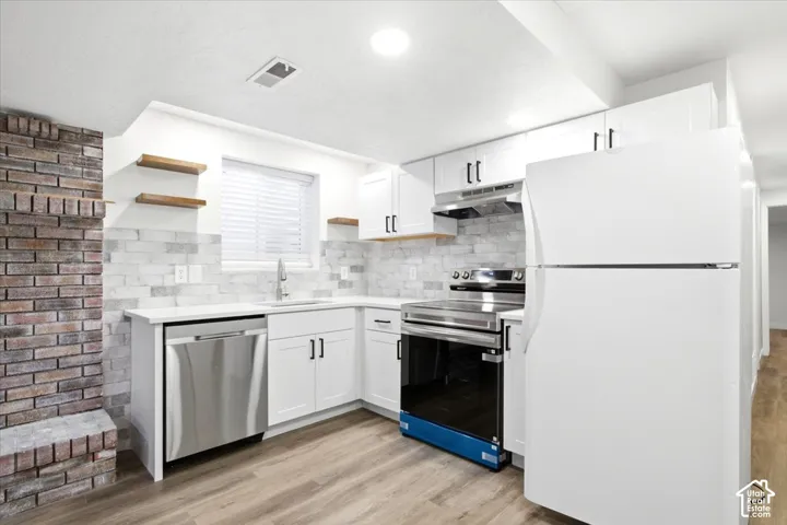 Bright  basement kitchen featuring white cabinetry, a white countertop, a tile backsplash, and stainless steel appliances
