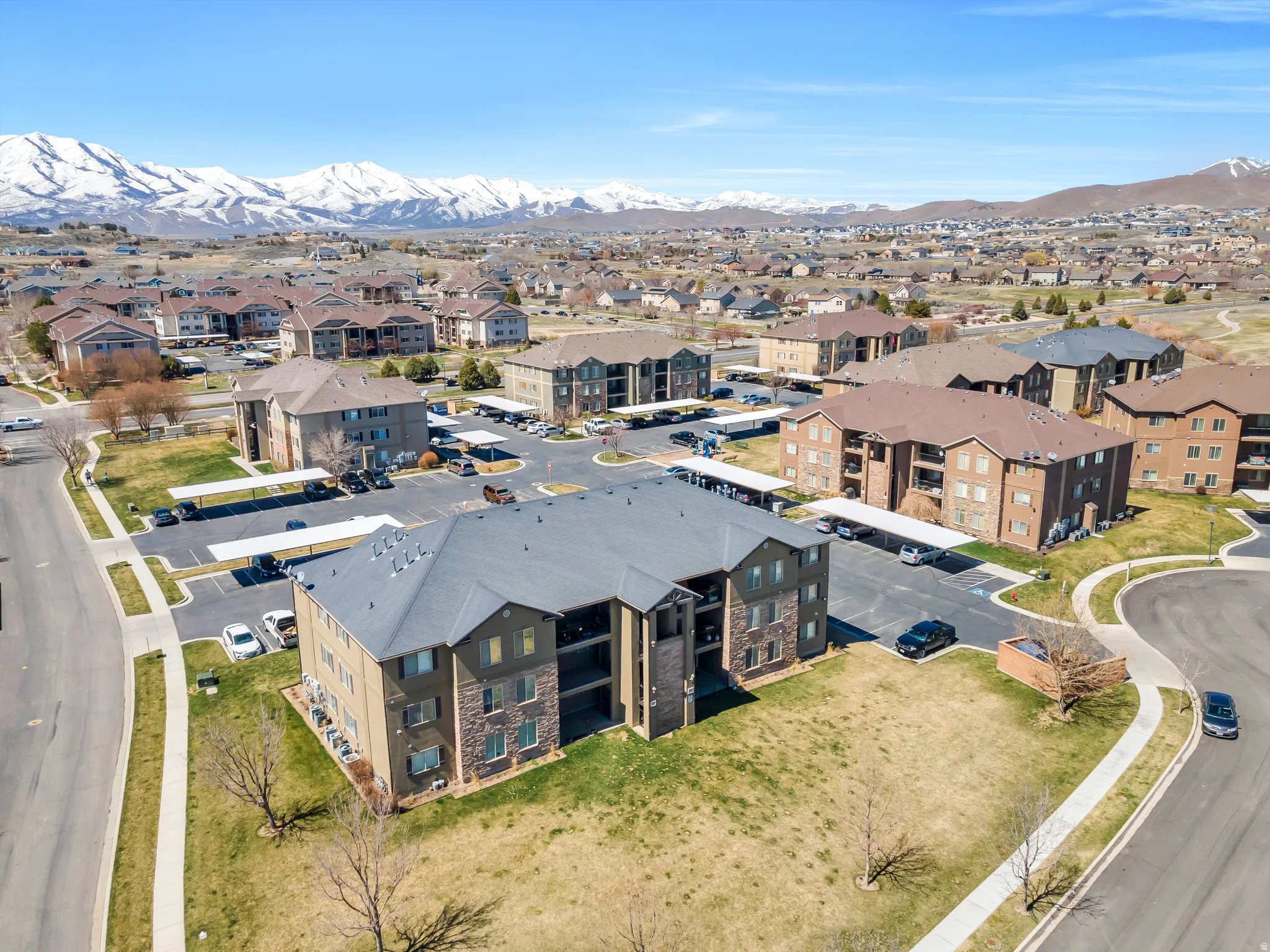 Multi-story residential buildings with tan siding and stone accents situated in a community featuring covered parking structures